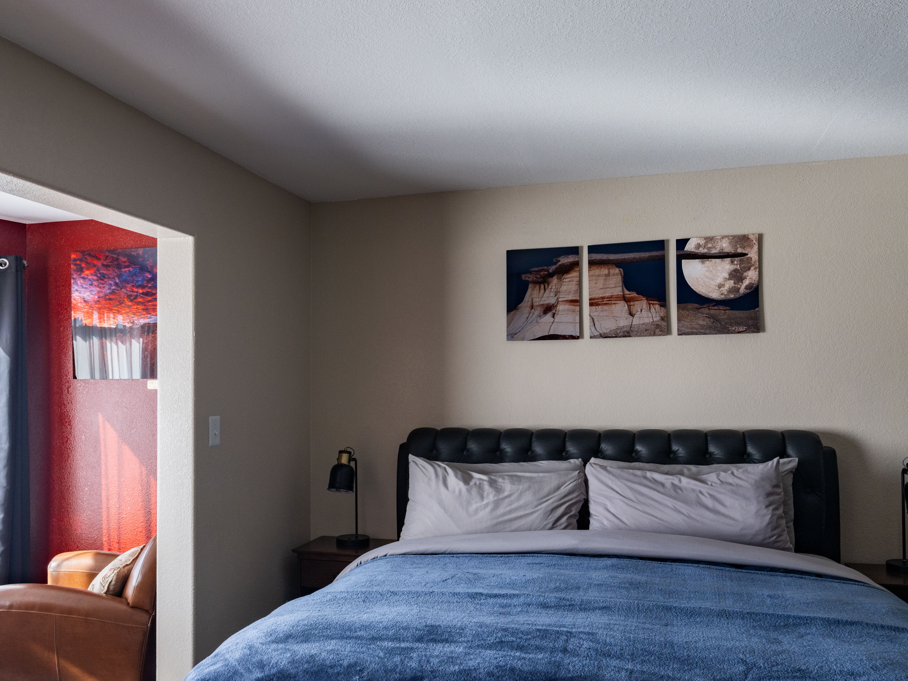 Une chambre à coucher avec un lit, une table de chevet, une lampe et un mur orné de trois tableaux.