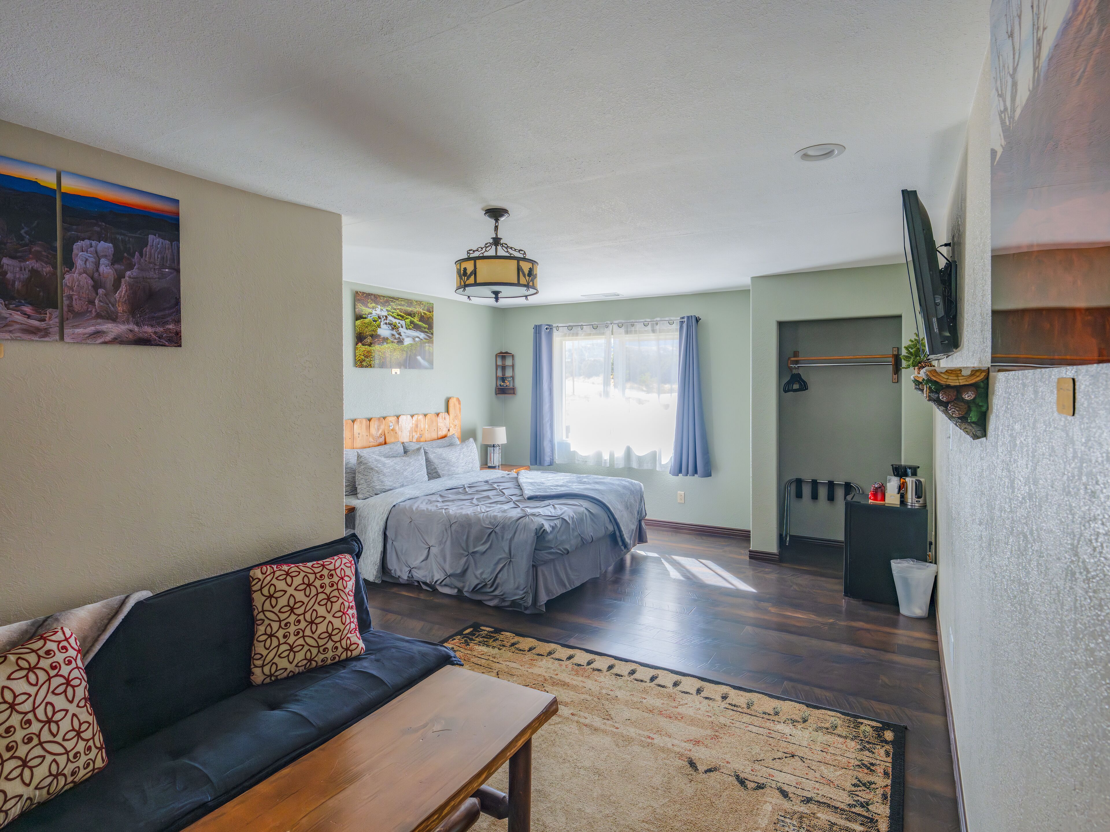 A bedroom with two beds, a sofa, a wooden bench, a rug, and a TV mounted on the wall.