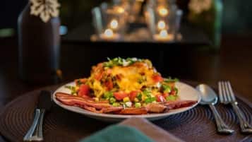 A plate of food with bacon, cheese, and vegetables on a table with candles in the background.