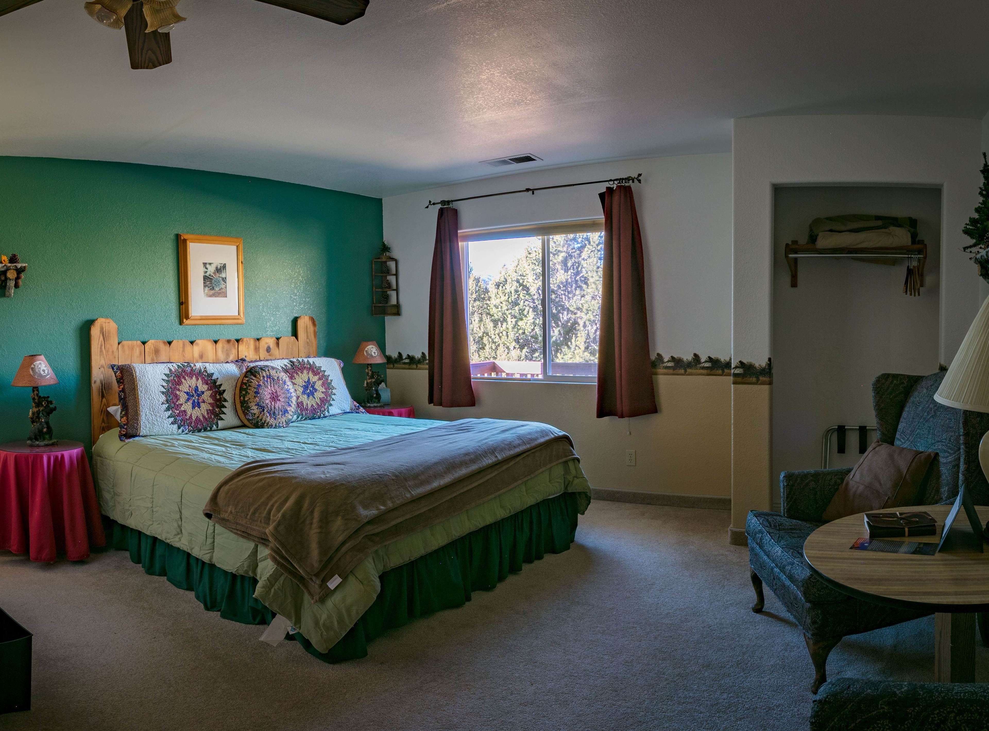 A bedroom with a bed, a window with curtains, a chair, and a lamp.