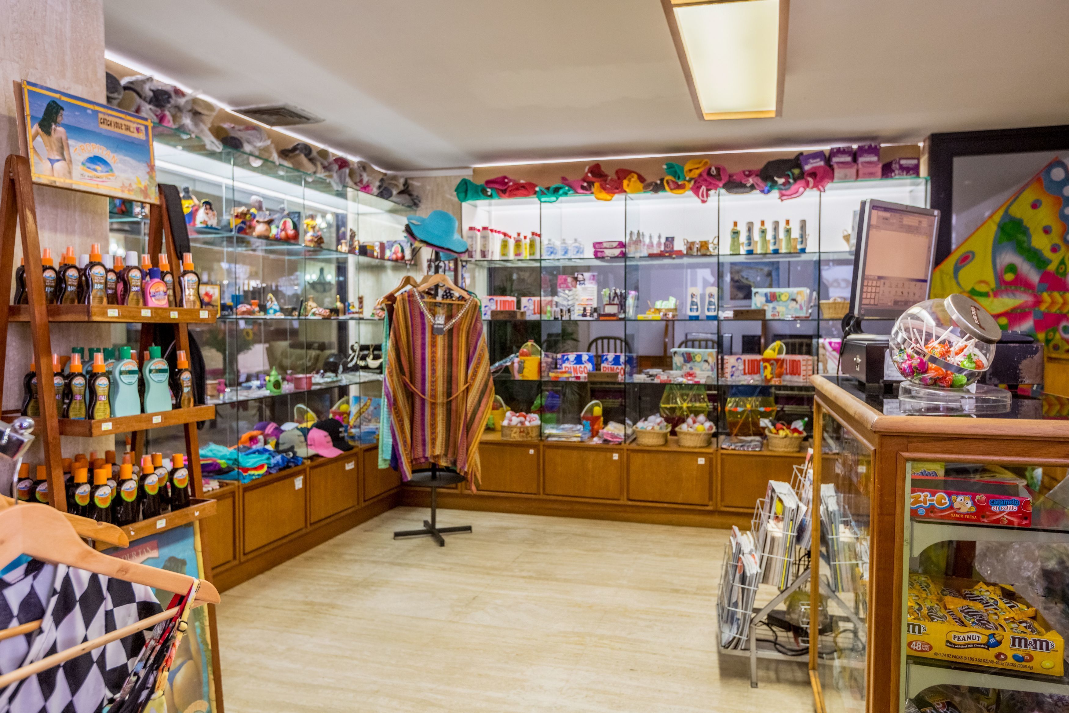 Una tienda con estantes llenos de diversos artículos, una computadora y una exhibición de sombreros coloridos.