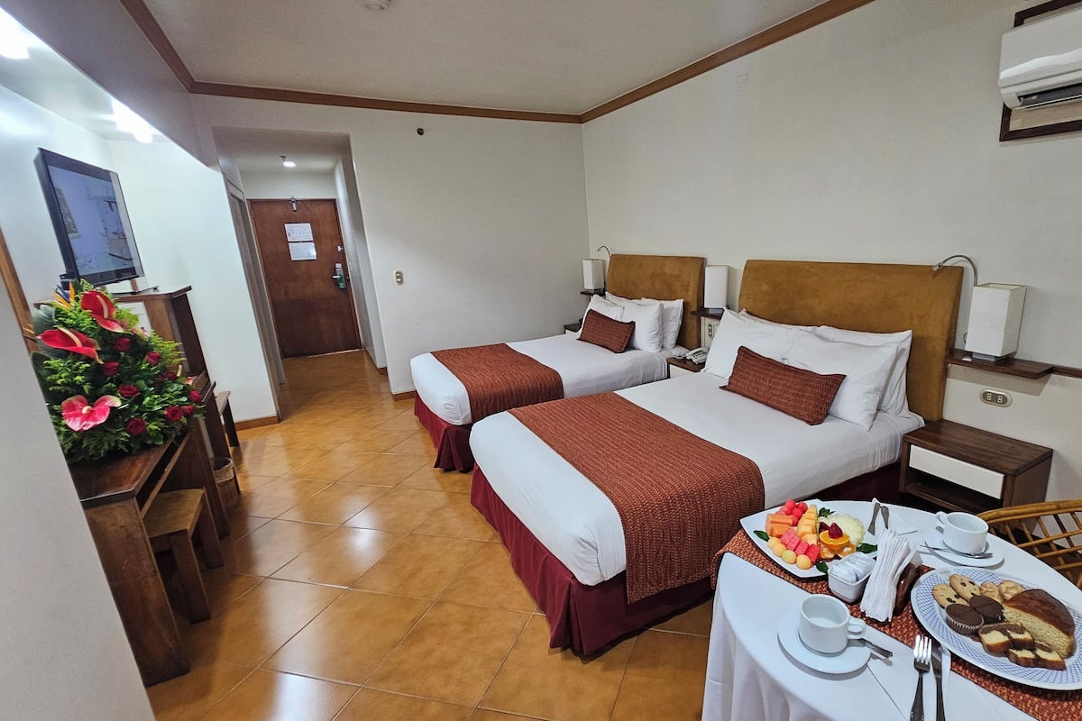 A hotel room with two beds, a dining table with breakfast, and a TV in the corner.
