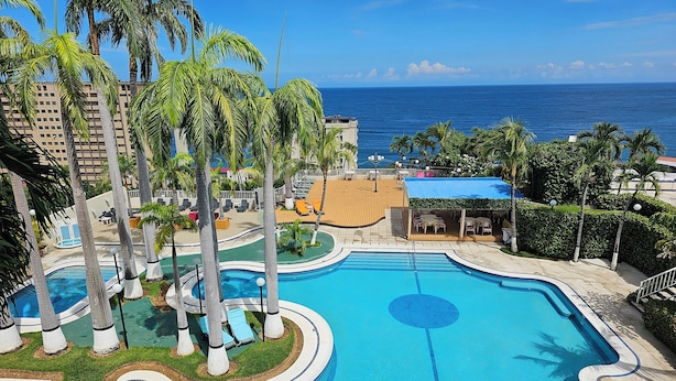 A swimming pool with a circular design, surrounded by palm trees and lounge chairs. - Hotel Ole Caribe (Macuto)