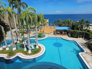 En pool med cirkelformad design, omgiven av palmer och solstolar.
