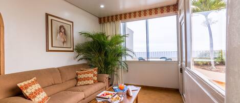 Una sala de estar con sofá, mesa de centro y un ventanal con vista a palmeras.