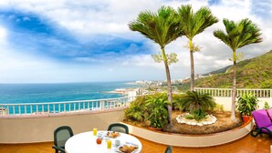 A terrace with a table set for dining, overlooking a coastal view with palm trees and a distant cityscape. - Hotel Ole Caribe (Macuto)