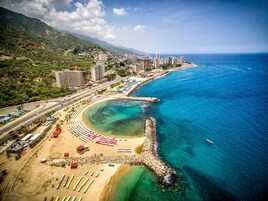 Vista aérea de una ciudad costera con playa, aguas azules cristalinas y una combinación de edificios residenciales y comerciales.