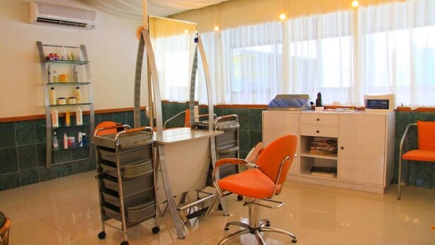 A salon with a white desk, orange chairs, and a metal shelf with toiletries. - Hotel Ole Caribe (Macuto)