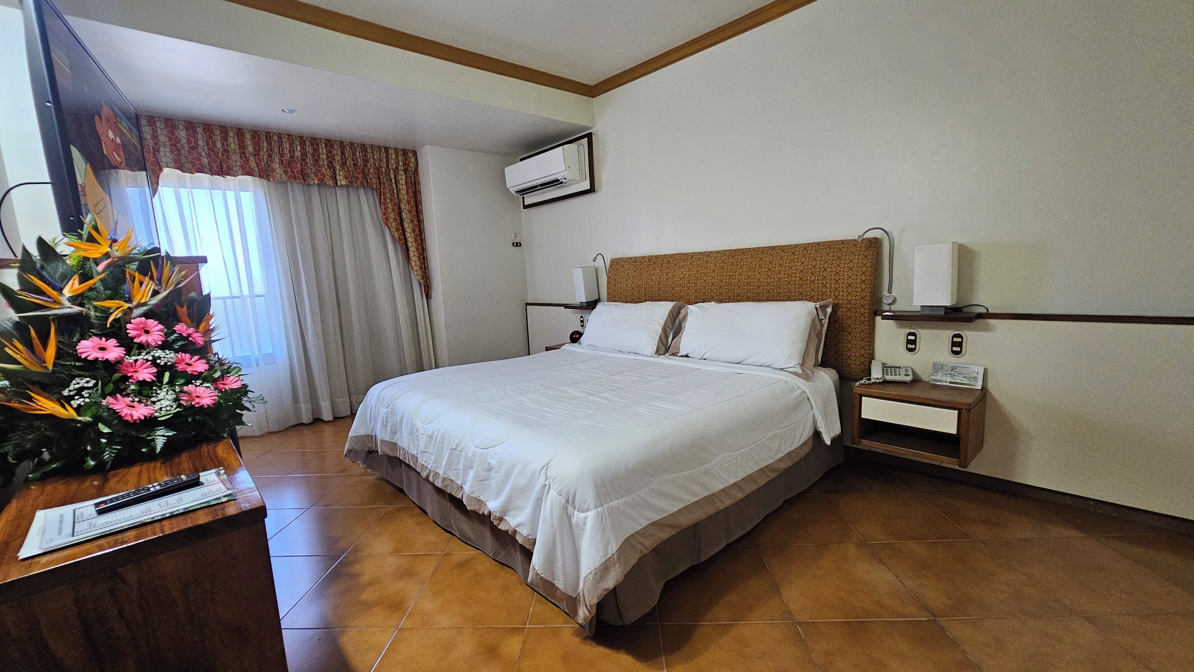 Een hotelkamer met een groot bed, een bureau met telefoon en een decoratieve plant.