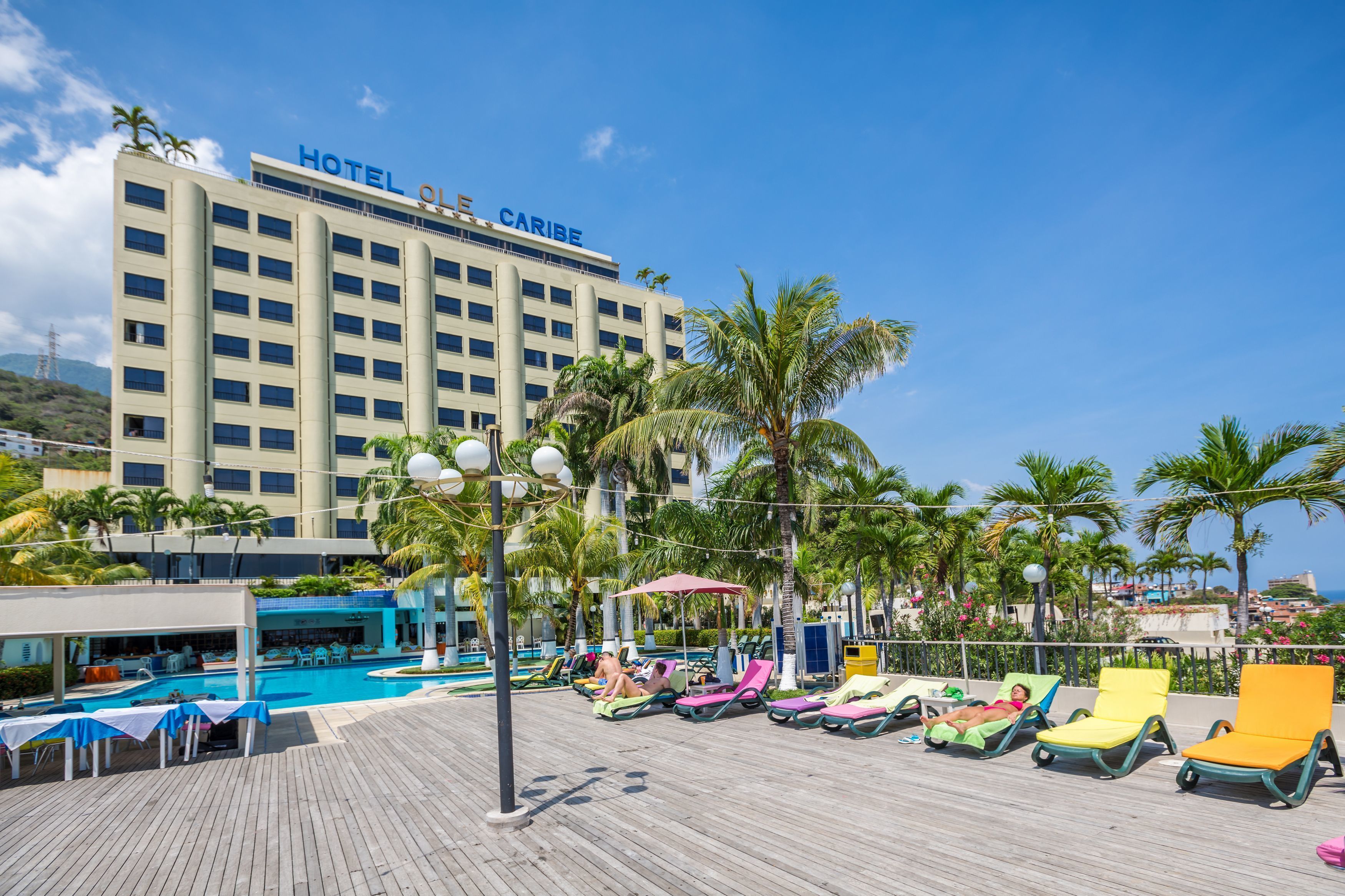Un hotel con piscina, sillas de descanso y palmeras.