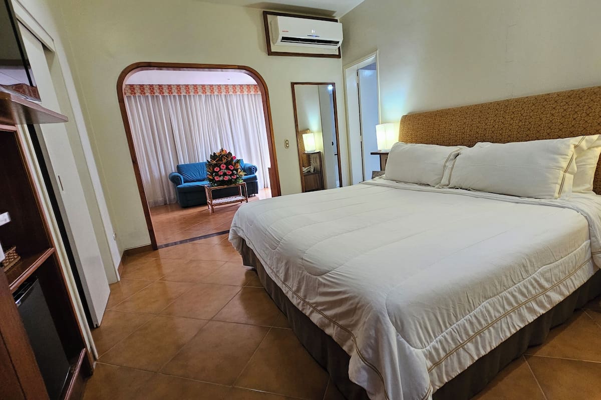 A hotel room with a large bed, a wardrobe, a bathroom, and a small seating area with a blue sofa and flowers.
