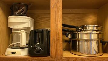 A kitchen cabinet with a coffee maker, toaster, and pots.