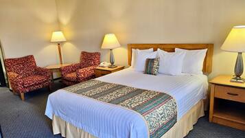 A hotel room with a large bed, two armchairs, a nightstand with a lamp, and a bedside table with a lamp.
