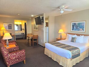 Ein Hotelzimmer mit einem Bett, zwei Stühlen, einem Schreibtisch, einem Fernseher und einem Deckenventilator.