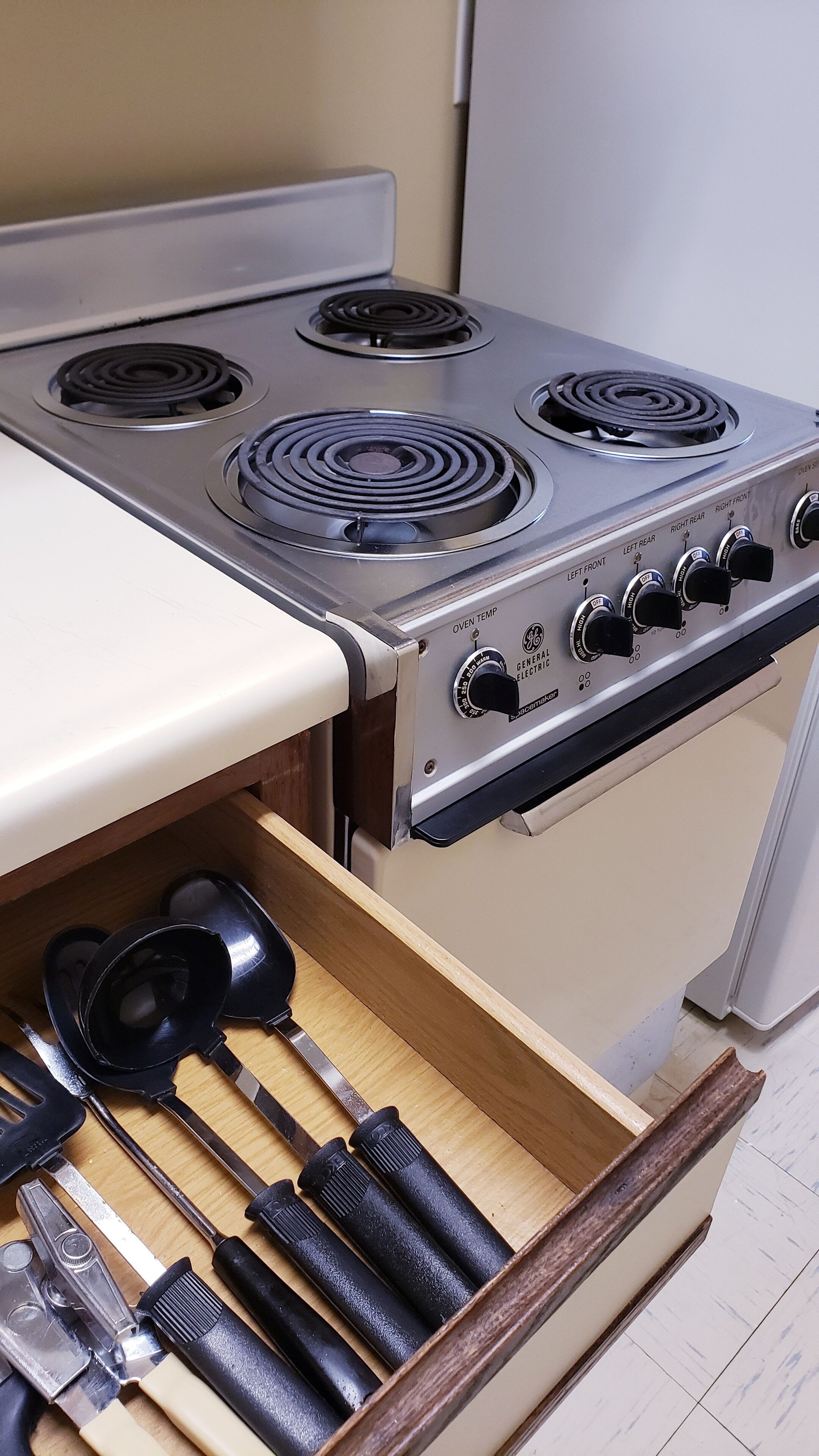 A kitchen with a stove, oven, and a drawer containing kitchen utensils.