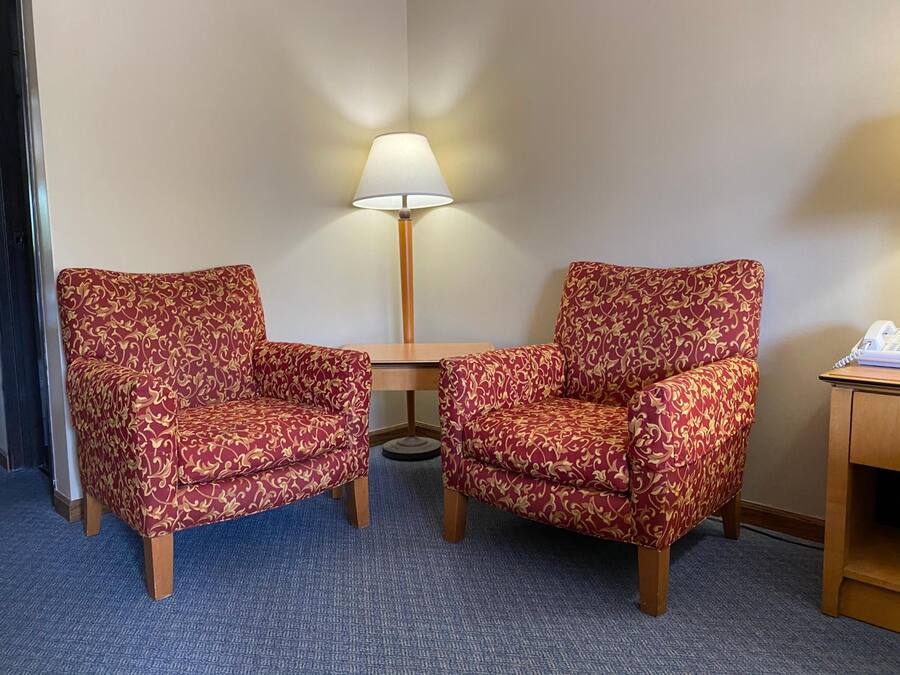 Deux fauteuils ornés d’un motif rouge et doré, une petite table, une lampe et un téléphone posés sur un bureau.