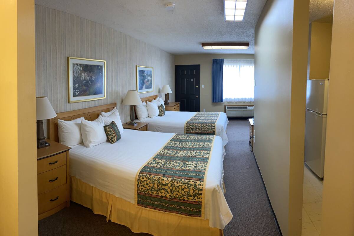 A hotel room with two beds, a desk, a chair, a wardrobe, and a window with curtains.