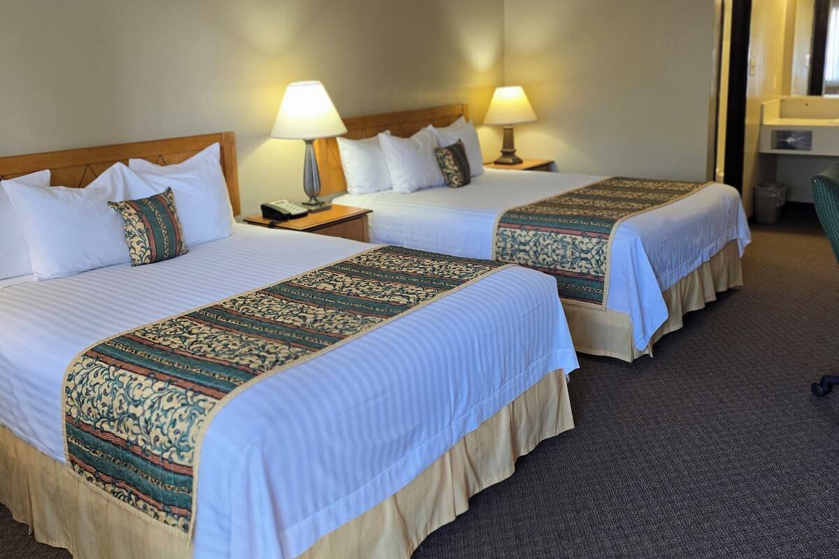 A hotel room with two beds, each with a patterned bedspread, bedside lamps, and a headboard.