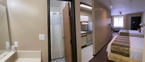 A hotel room with a bathroom, a kitchenette, and a bed.