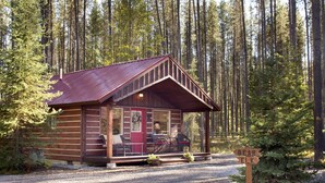 Een vakantiehuisje van hout met een veranda, een rode deur en een bord met aanwijzingen naar 'Bear' en 'Elk'.