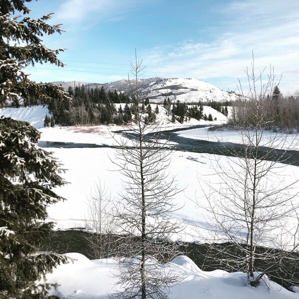 Un paisaje nevado con un río, árboles y montañas a lo lejos.