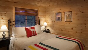 Een houten slaapkamer met een bed, twee nachtkastjes, een raam met zonwering en twee lijstjes met posters aan de muur.