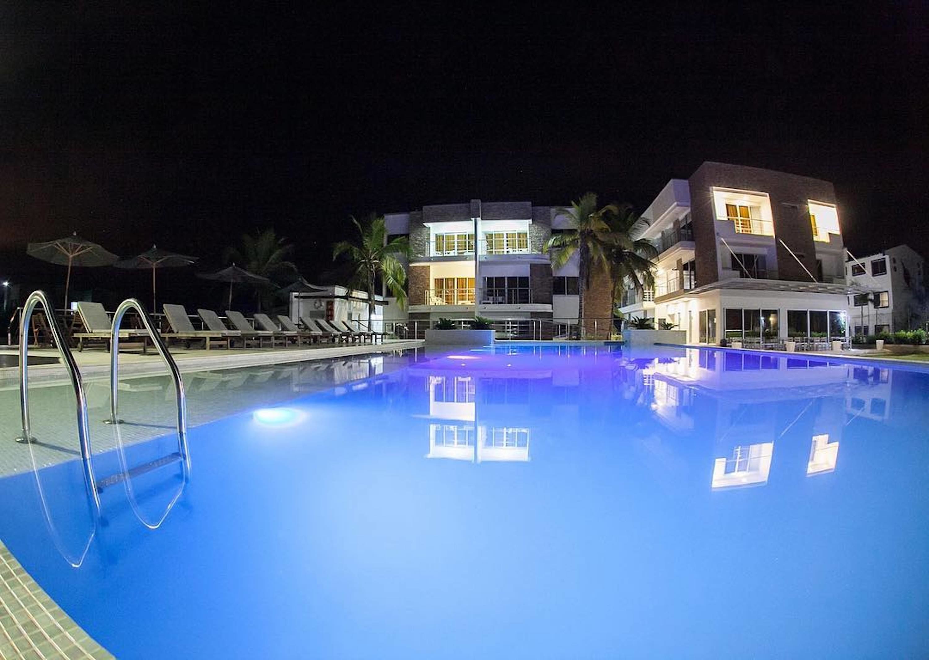 A swimming pool with lounge chairs and umbrellas, surrounded by modern buildings with large windows and balconies.