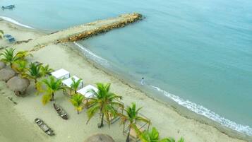 Una playa con cabañas de techo de paja, palmeras y un muelle que se adentra en el agua.