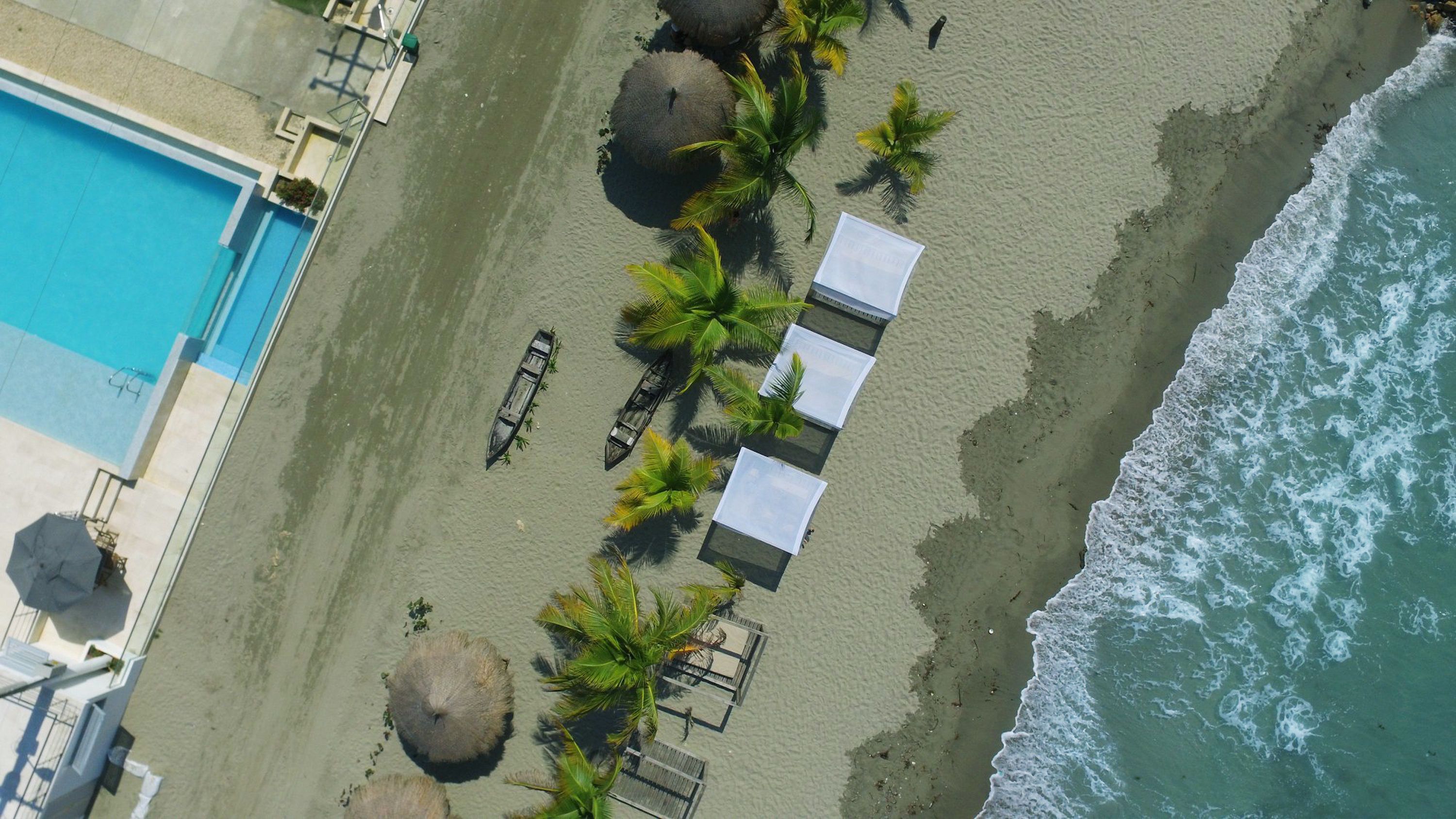 Vue aérienne d’un hôtel situé en bord de mer, avec une piscine, des palmiers et des parasols de plage.