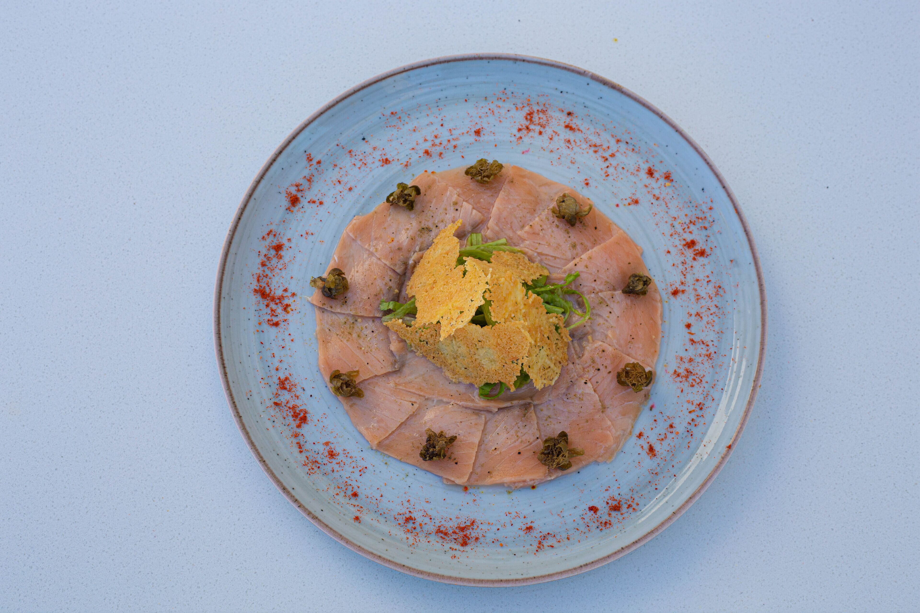A plate with sliced salmon, a dollop of yellow sauce, and green garnish on a blue plate.