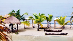 A beach with thatched umbrellas, lounge chairs, and palm trees. -  Loa Tolú by Bernalo Hotels (Tolú)