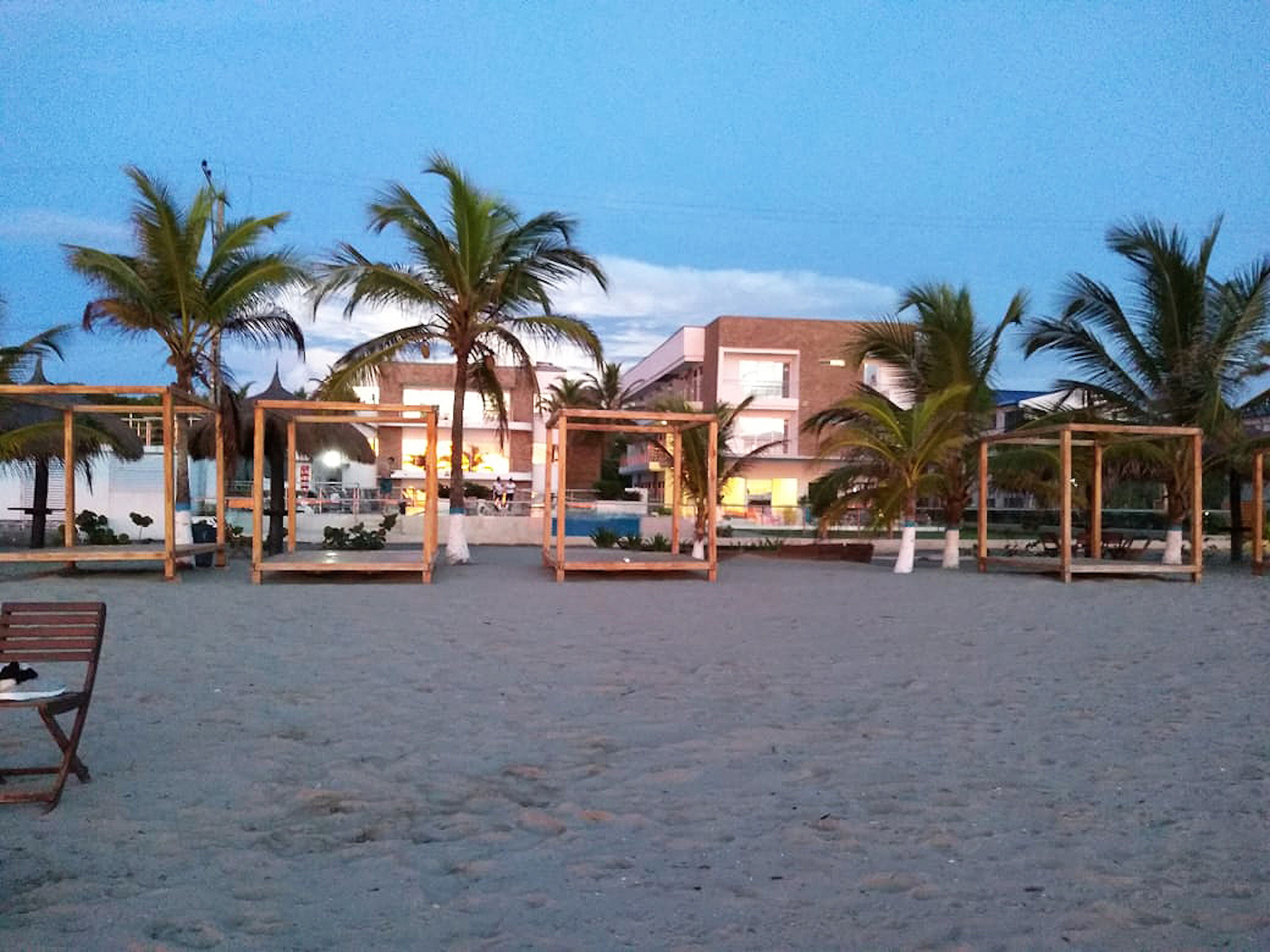 A beach with wooden structures, palm trees, and a building in the background.