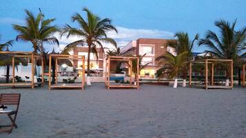 A beach with wooden structures, palm trees, and a building in the background.