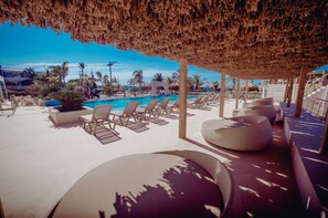 A poolside area with lounge chairs and a thatched roof structure.