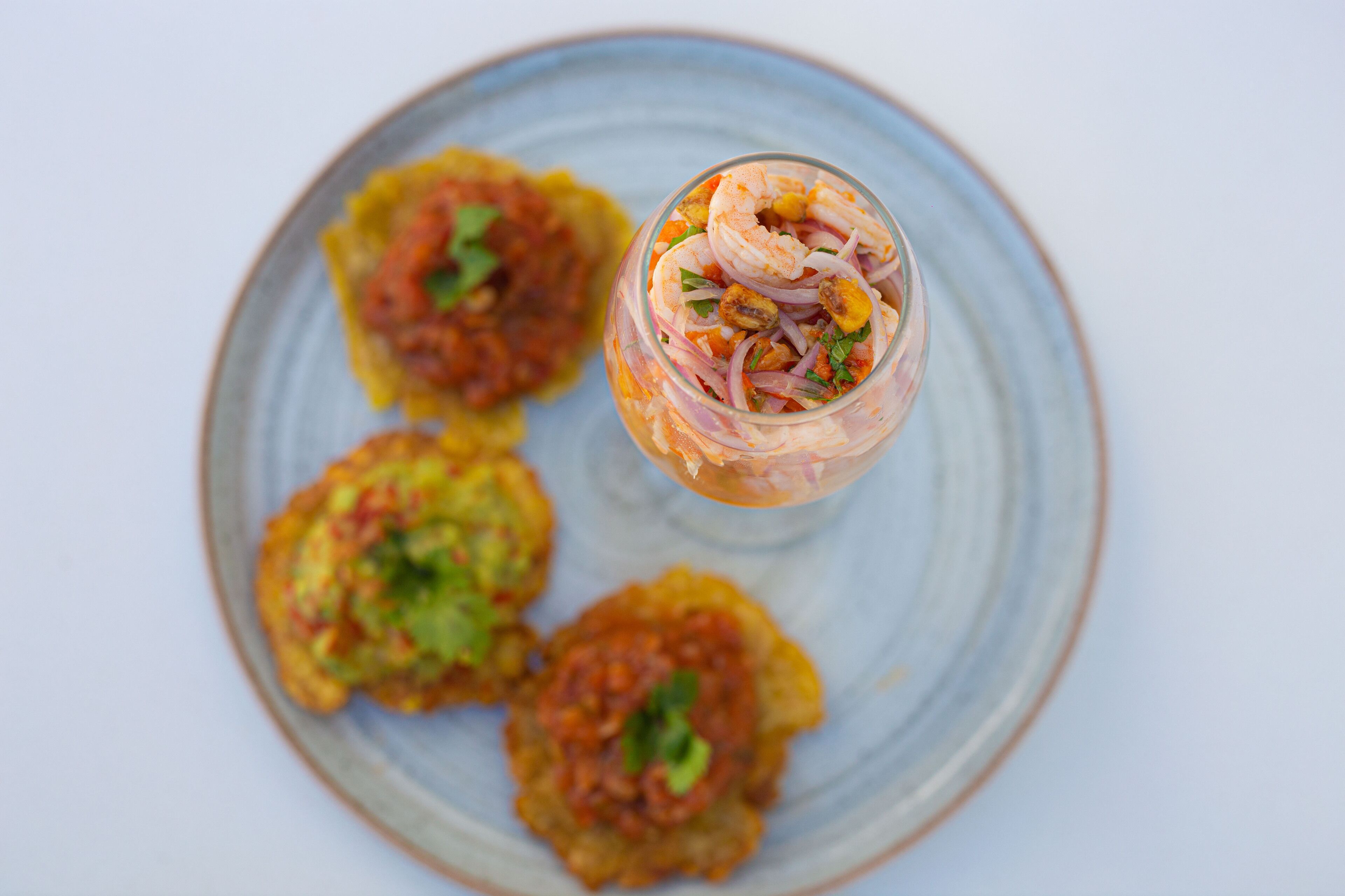 A plate with four food items and a glass containing a shrimp cocktail.