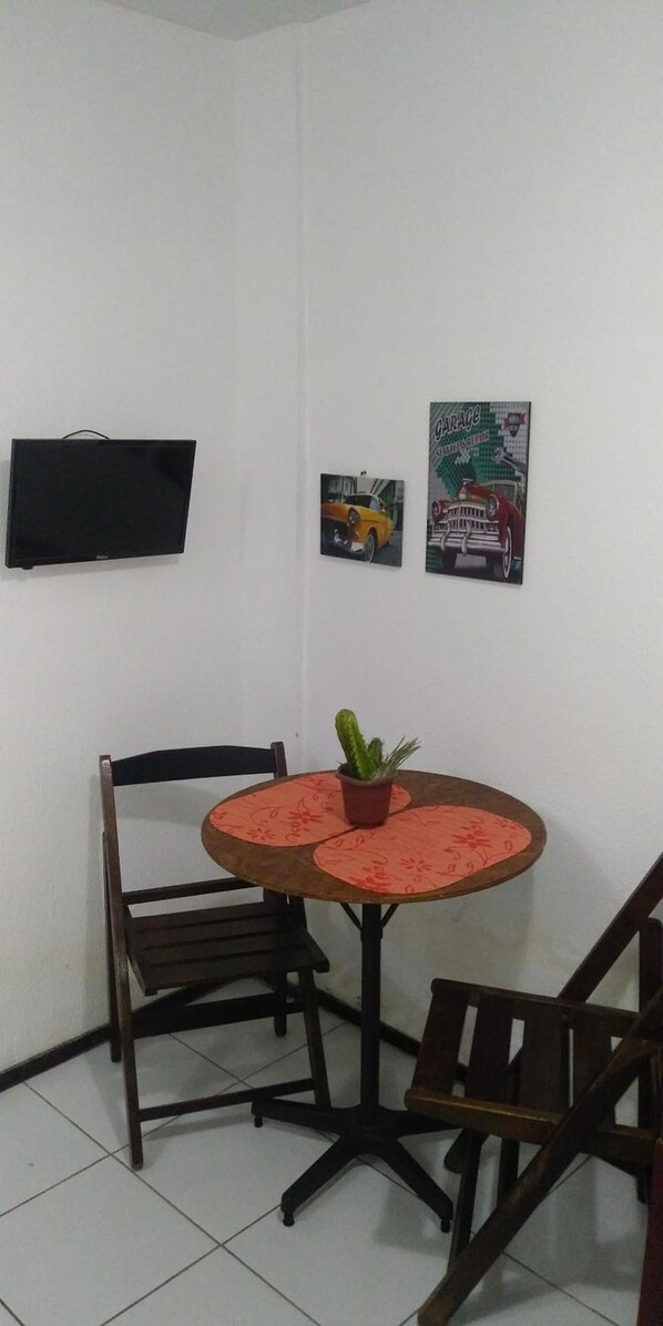 A small dining area with a round table, two chairs, a potted plant, and two wall-mounted posters. - Studio Piedade (Jaboatão dos Guararapes)