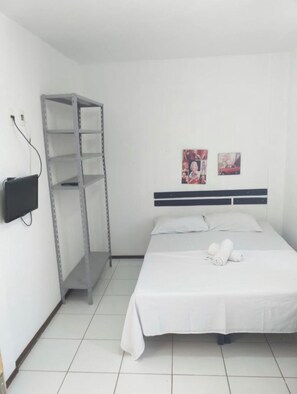 A hotel room with a bed, a metal shelf unit, a flat-screen TV, and two wall-mounted pictures. - Studio Piedade (Jaboatão dos Guararapes)