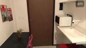 A small room with a single table, a chair, a microwave, and a door. - Studio Piedade (Jaboatão dos Guararapes)
