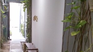 A narrow corridor with a bench, a wall-mounted light fixture, and climbing plants. - Studio Boa Viagem (Recife)