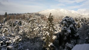 A snowy mountain landscape with dense forest and a house in the foreground. - Hosteria Pajaro Azul (San Carlos de Bariloche)