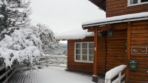 A wooden cabin with a snow-covered deck and a wooden fence. - Hosteria Pajaro Azul (San Carlos de Bariloche)