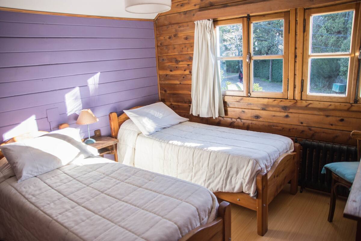 Une pièce avec deux lits en bois, une fenêtre avec des rideaux, un radiateur et une chaise.