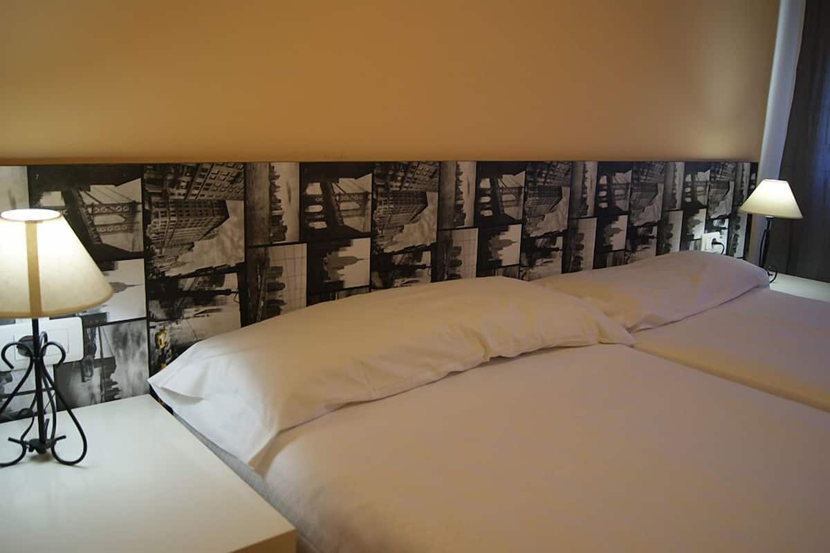 A hotel room with a bed, two bedside lamps, and a wall with a black and white abstract design.