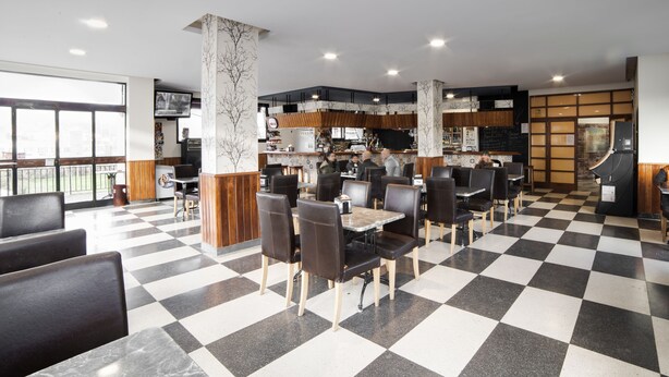 A modern restaurant with checkered flooring, black and white chairs, and a visible kitchen area. - Hotel San Blas (Abadino)