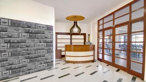 A reception area with a wooden reception desk, a wall of vintage suitcases, and a large sliding glass door leading to a spacious room. - Hotel San Blas (Abadino)