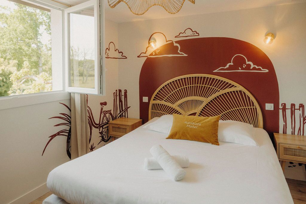 A hotel room with a bed, a window, a wall mural, and a nightstand.