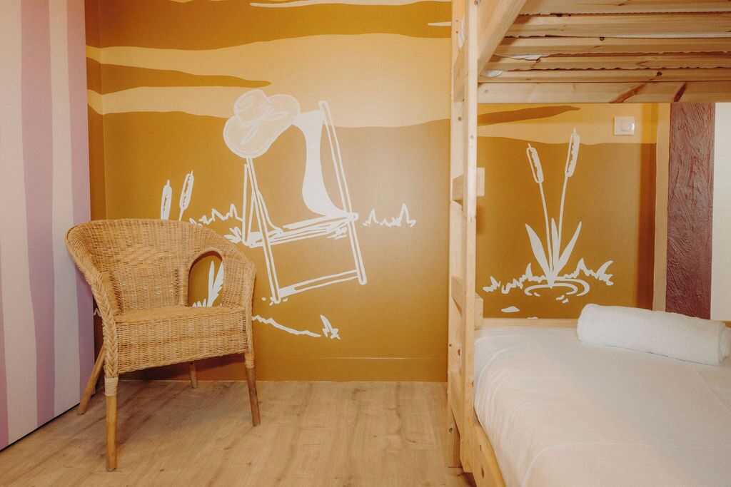 A room with a bed, a wicker chair, and a wall mural.