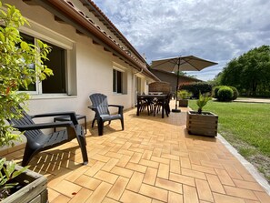 An outdoor patio with a tiled floor, a wooden table with chairs, a black plastic chair, and a wooden planter. -  Adishatz Motel (Biscarrosse)