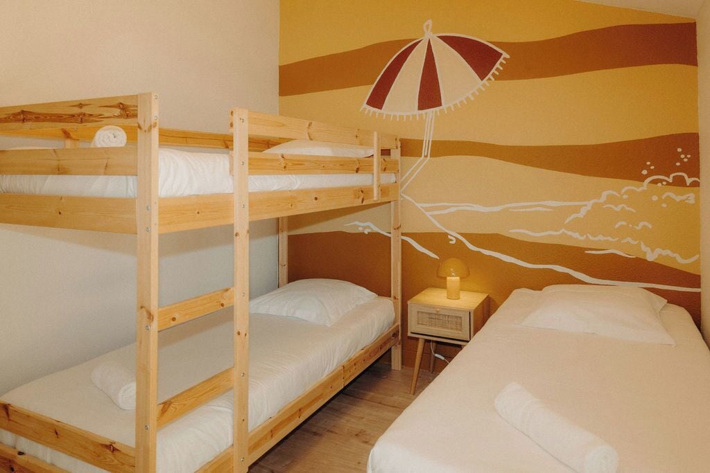 A bunk bed room with a beach-themed wall mural, a small bedside table with a lamp, and a wooden floor.