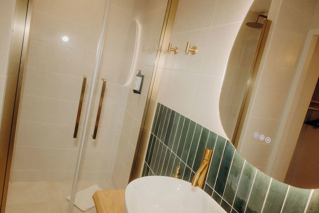 A bathroom with a white sink, a glass shower enclosure, and a green-tiled accent wall.